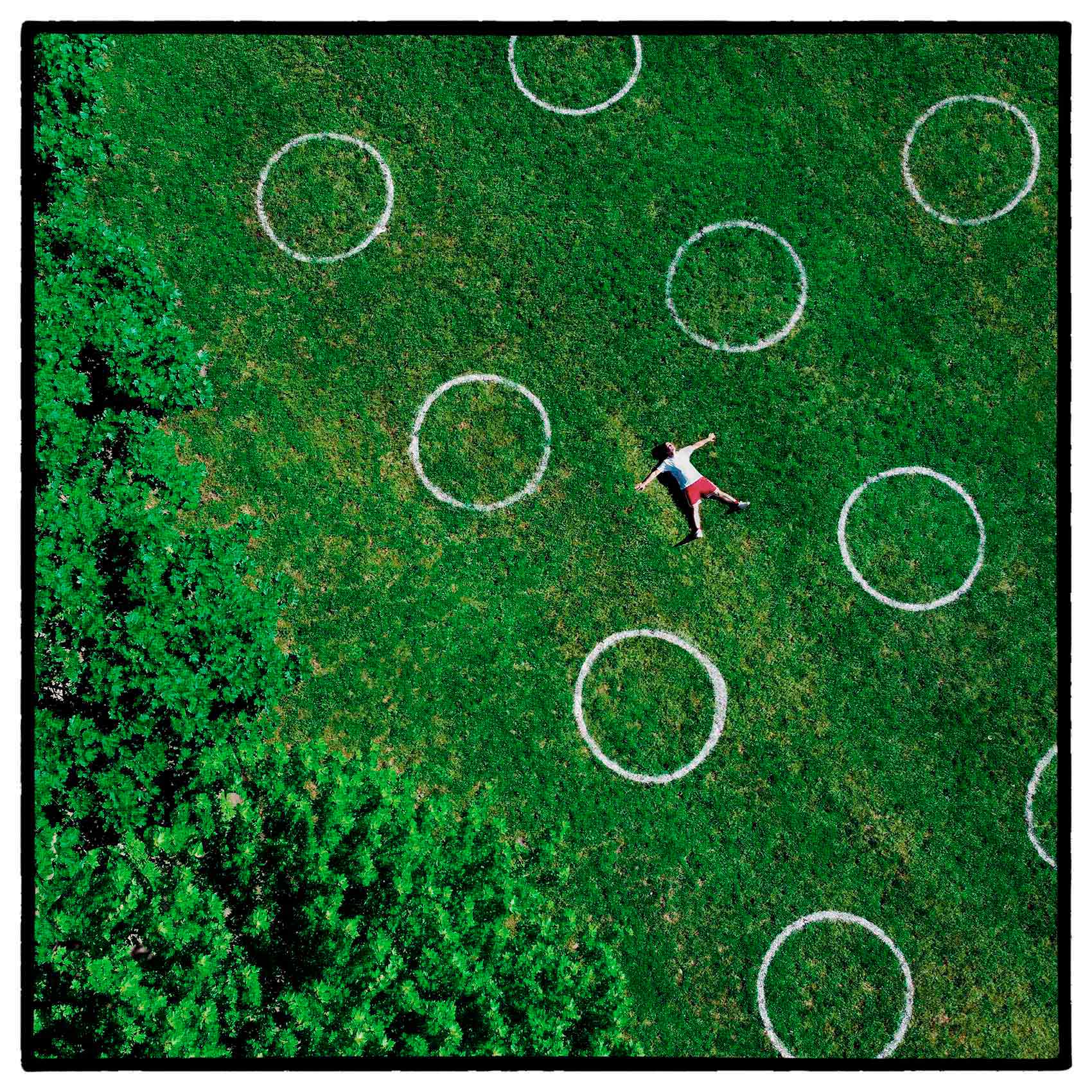 a man lays amongst the painted socially distance circles at trinity bellwoods park in toronto