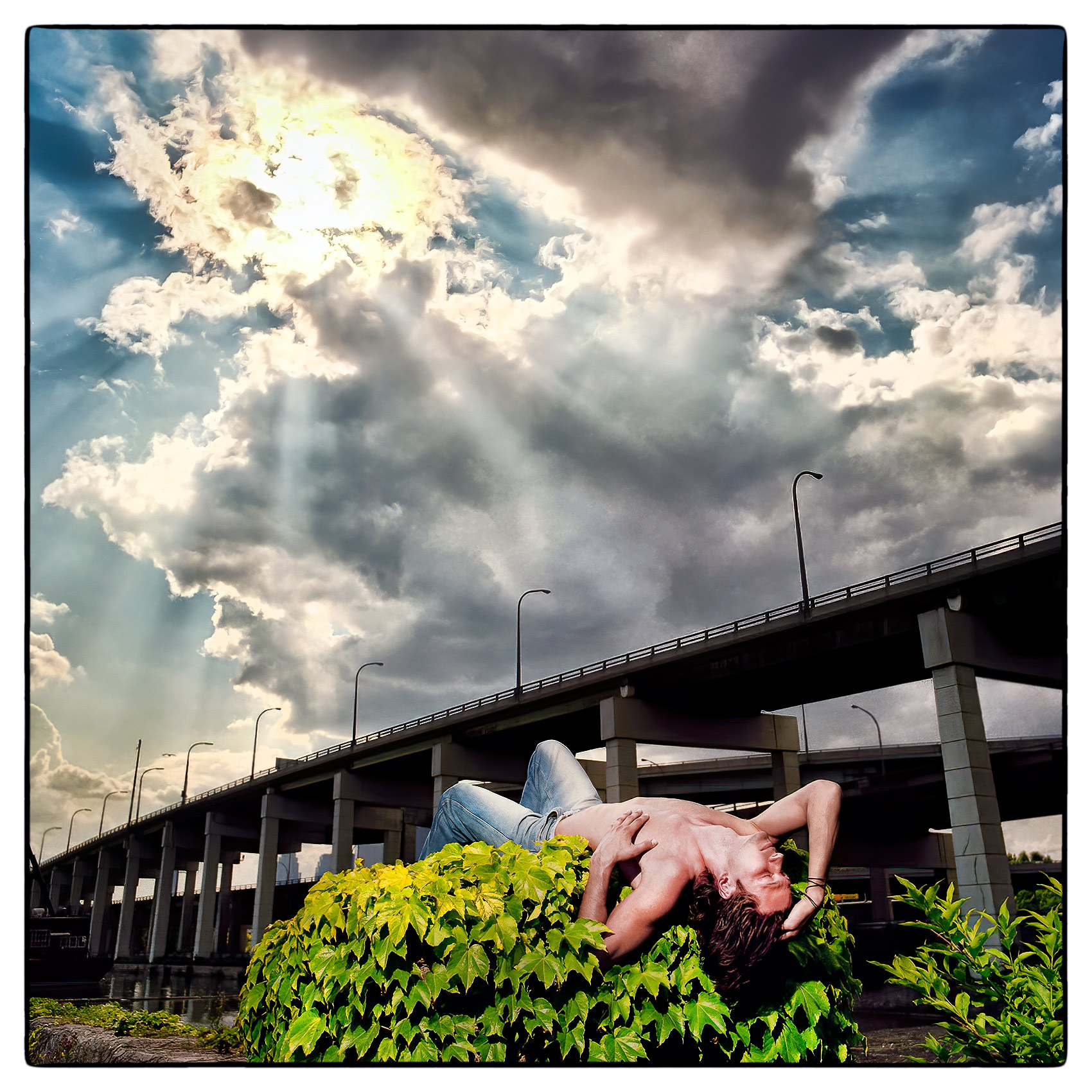a-male-model-poses-shirtless-on-top-of-a-concrete-pillar-next-to-torontos-gardiner-expressway