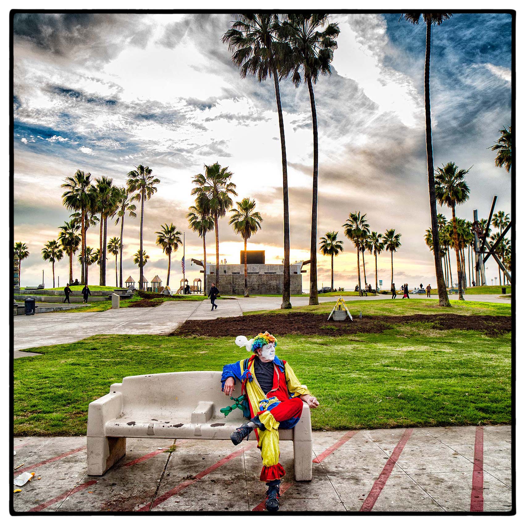 a-man-dressed-as-a-clown-sits-on-a-park-bench-in-venice-beach-california