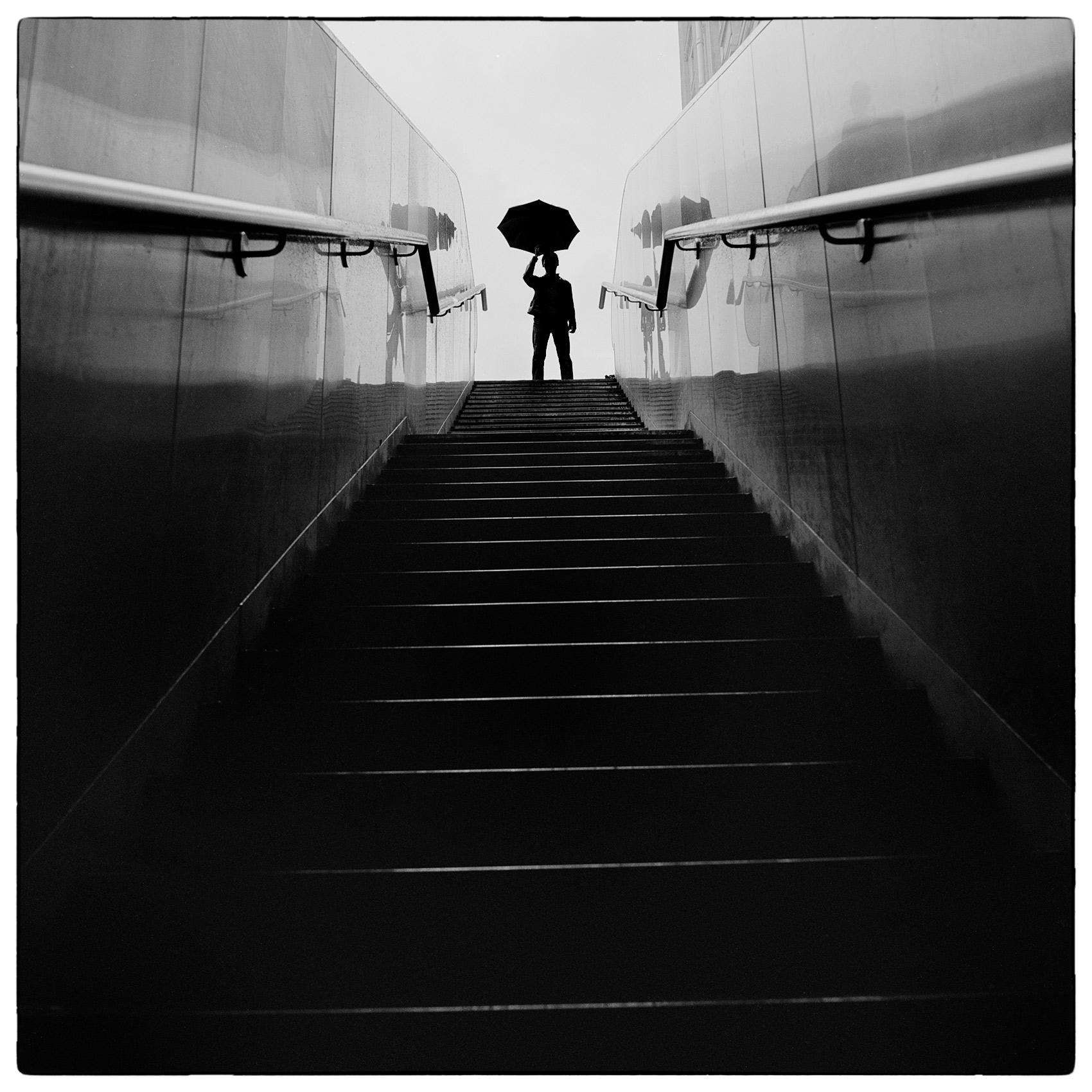 a-man-holding-an-umbrella-is-silhouetted-as-gets-ready-to-ascend-a-staircase-in-paris-france