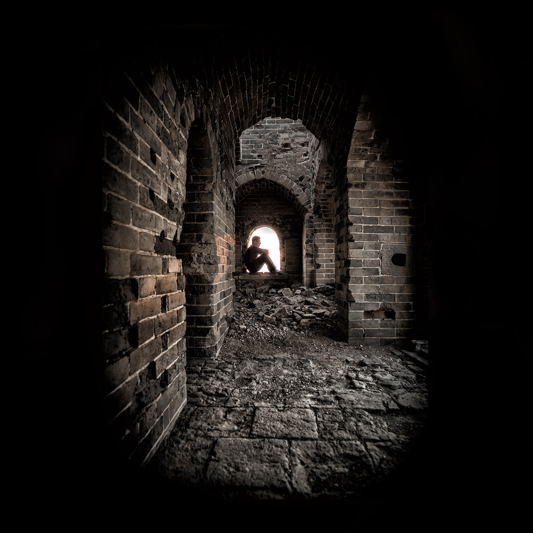 a-man-is-silhouetted-as-he-sits-inside-a-windowsill-in-an-ancient-guard-tower-on-the-great-wall-of-china