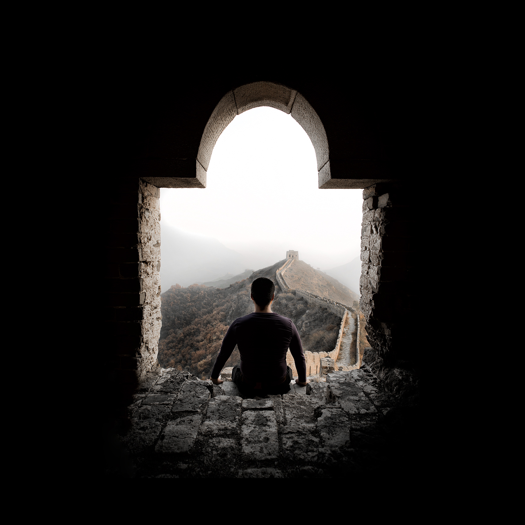 a man looks out at the great wall as he sits in one of the towers near simatai china
