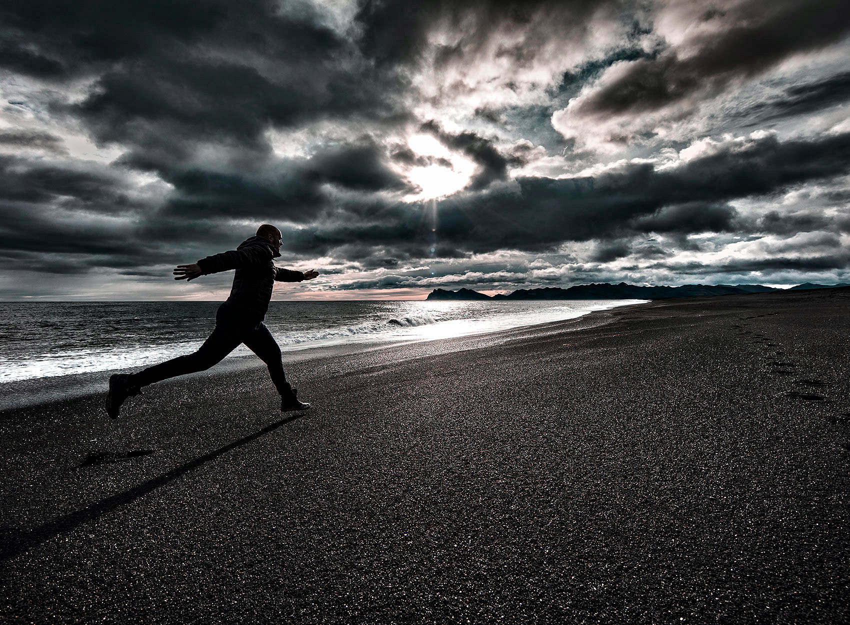 a man runs on an icelandic volcanic beach during an early fall sunset