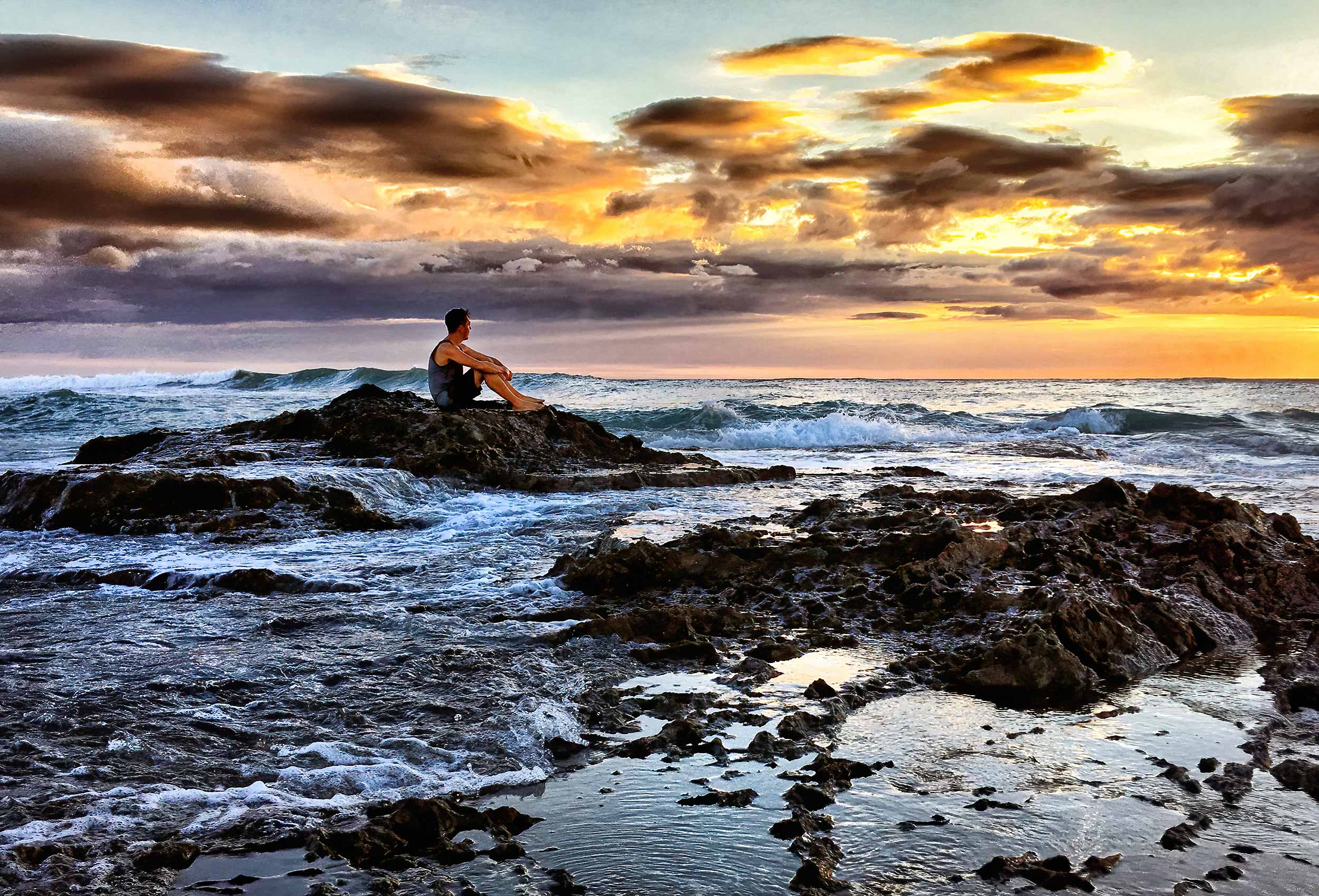 a-man-sits-on-a-rock-watching-a-sunset-by-an-editorial-photographer