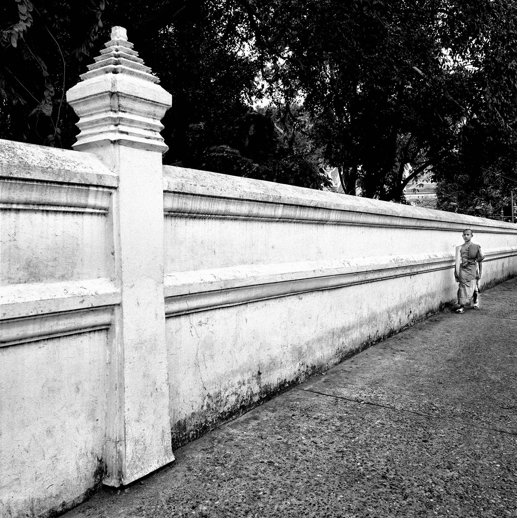 a-monk-is-dwarfed-by-a-long-white-wall-while-out-walking-in-bangkok-thailand