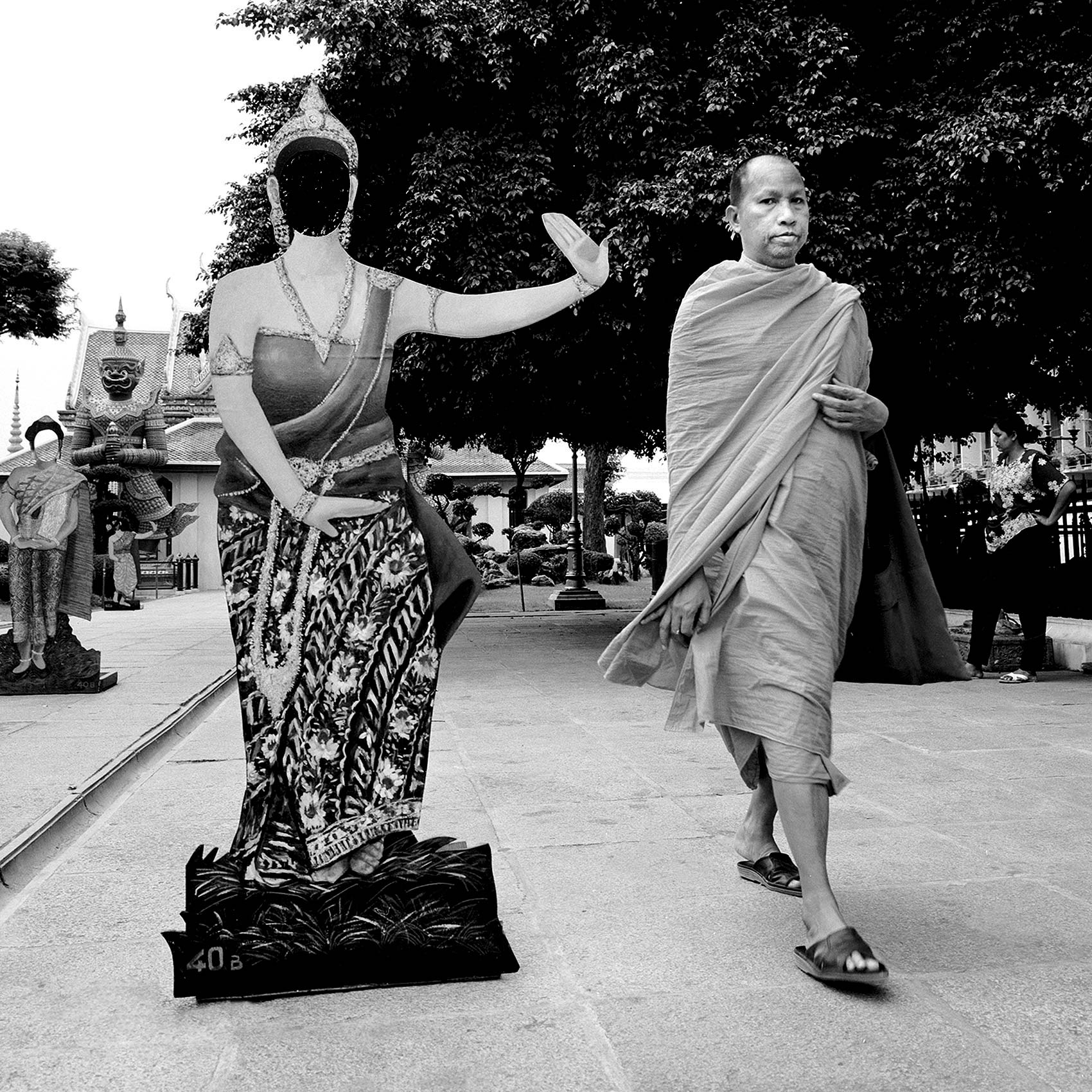 a-monk-walks-past-a-life-size-cut-out-of-a-thai-woman-in-traditional-dress-in-bangkok