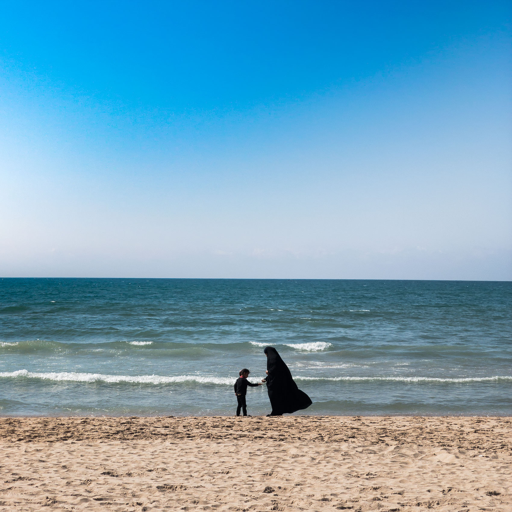 a muslim woman wearing a burqua plays with her daughter on a beach in beirut