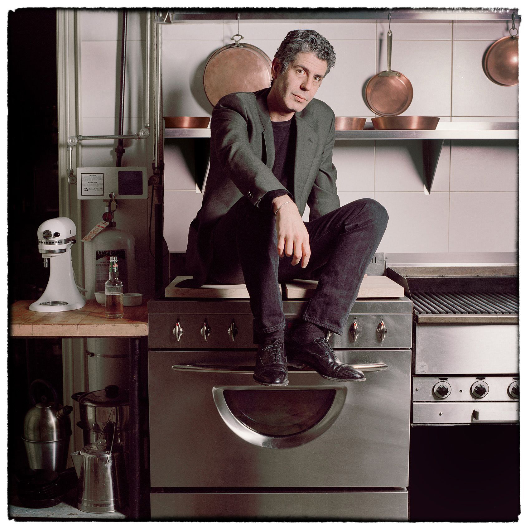 celebrity chef anthony bourdain poses for a photo while sitting on a stove in a toronto kitchen