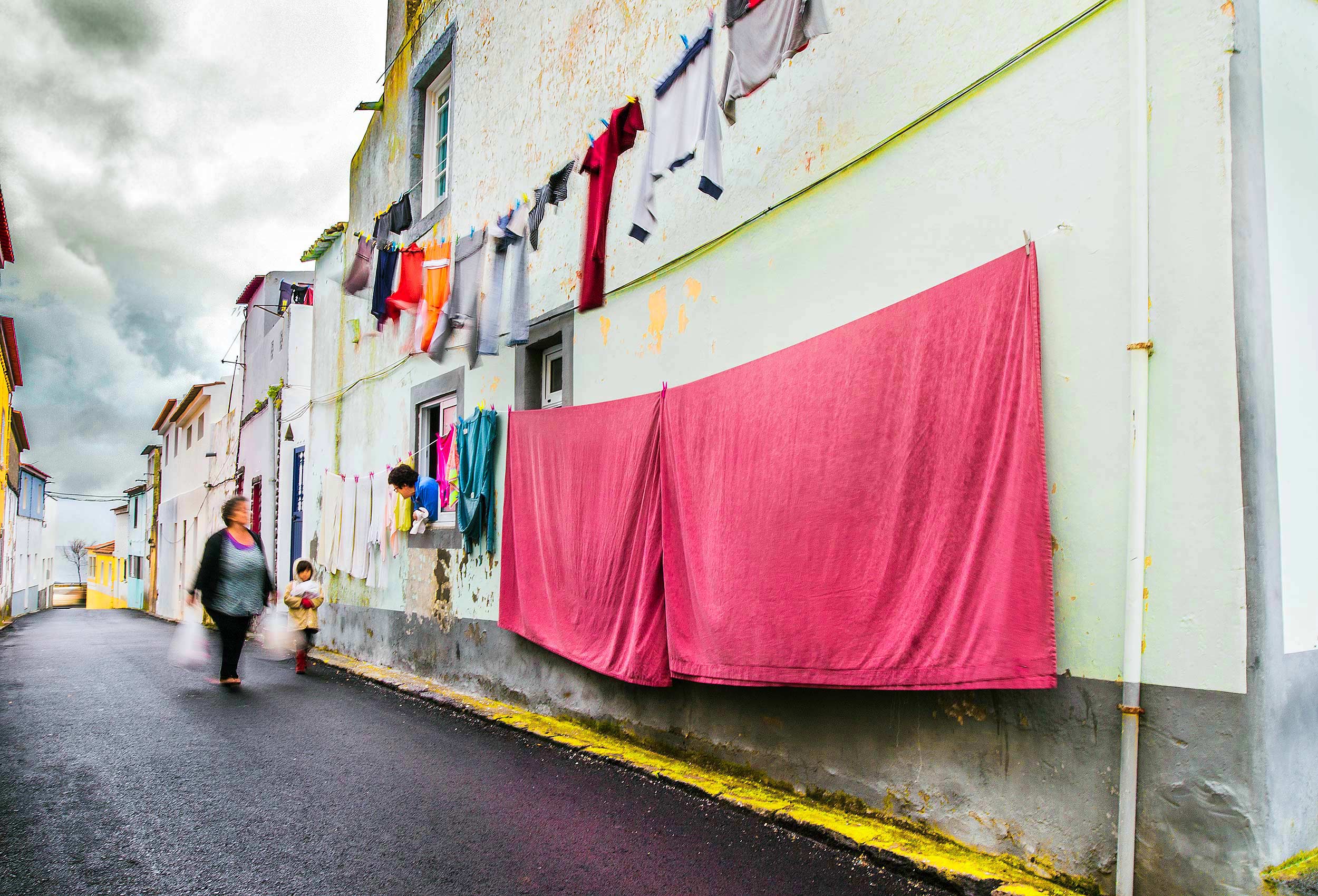 a-woman-hanging-laundry-talks-to-neighbors-on-the-street-in-ponta-delgada-azores-portugal