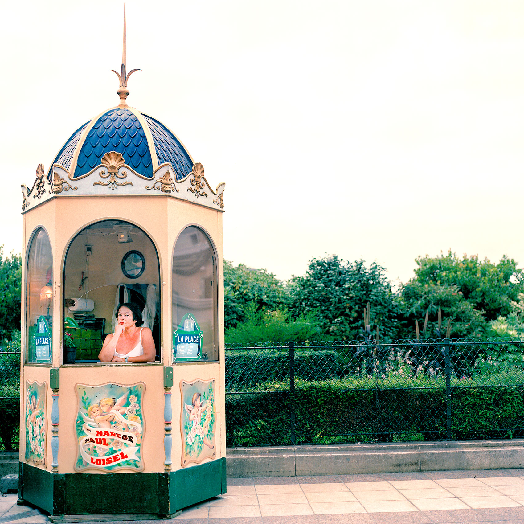 a woman waits in her ornate ticket booth for merry go round customers in paris 