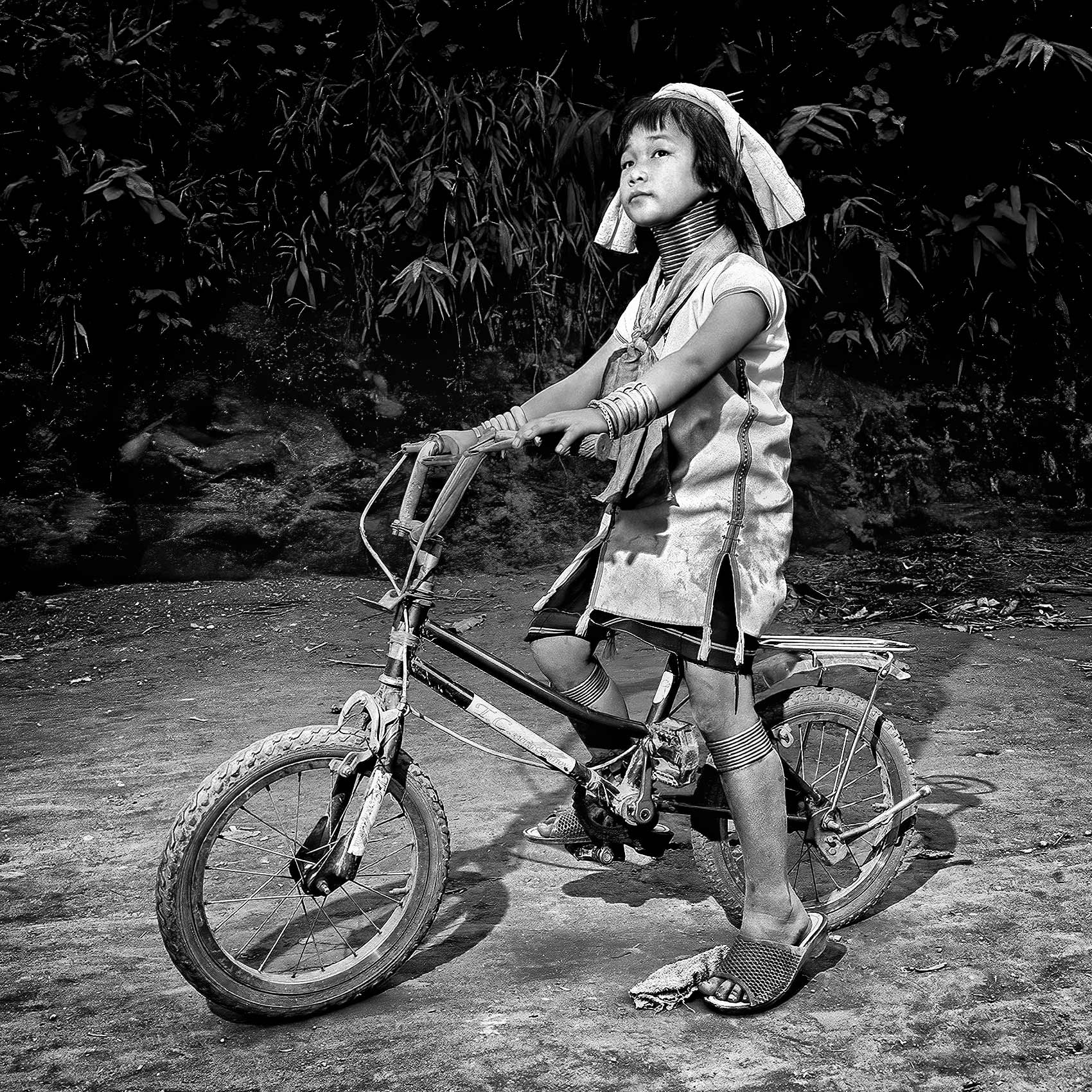 a young girl from the karen tribe poses for a photo in the long neck village on her bicycle in northern thailand