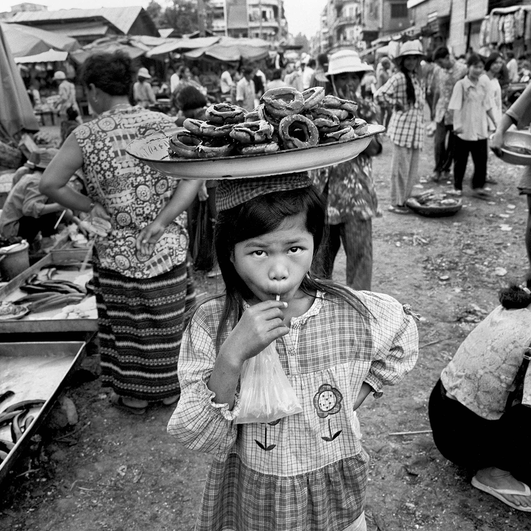 a-young-girl-in-an-angkor-wat-market-tries-to-sell-donuts-balanced-in-a-tray-on-her-head