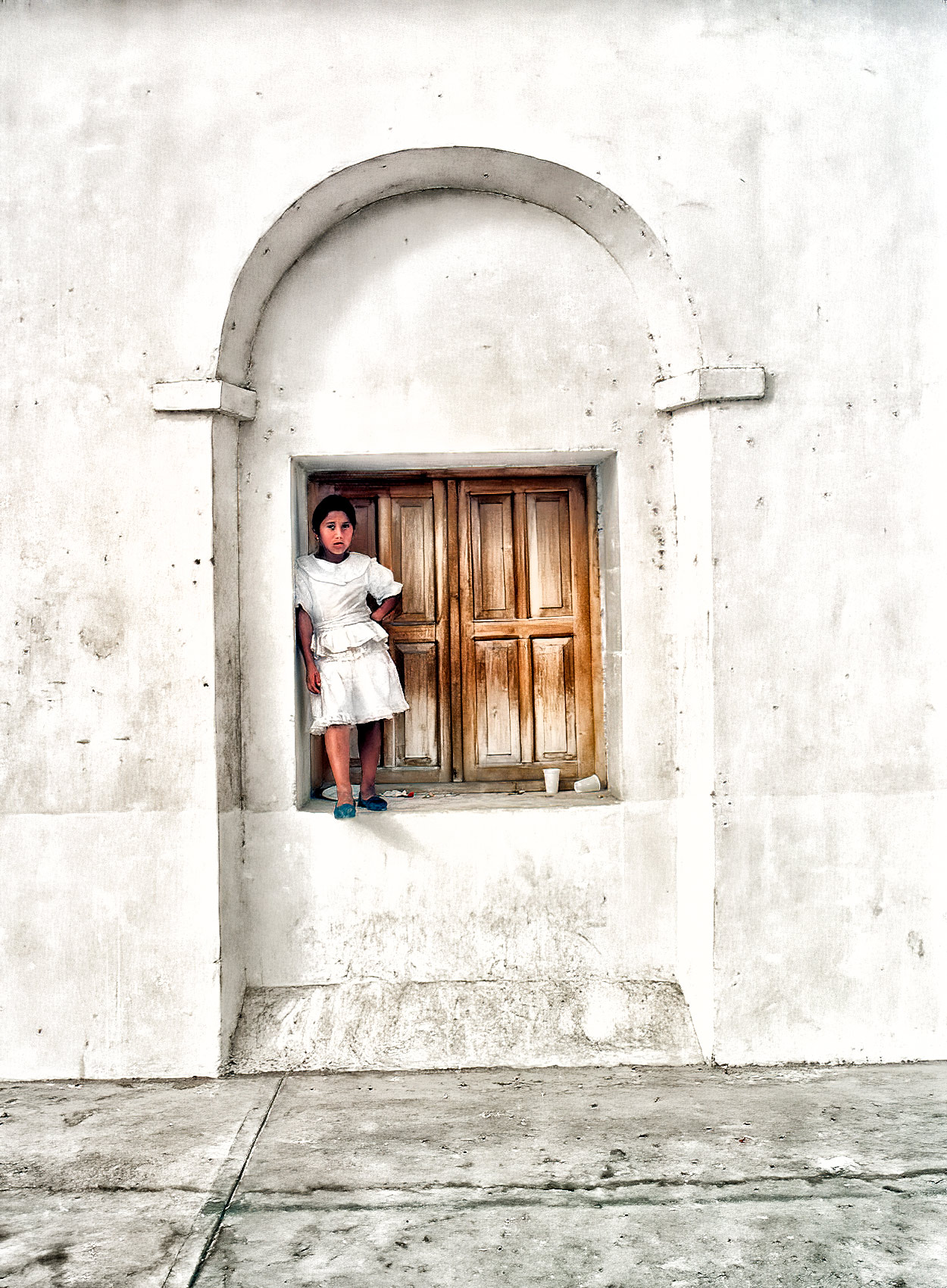 a young guatemalan girl stands in a windowstill watching a festival in flores 
