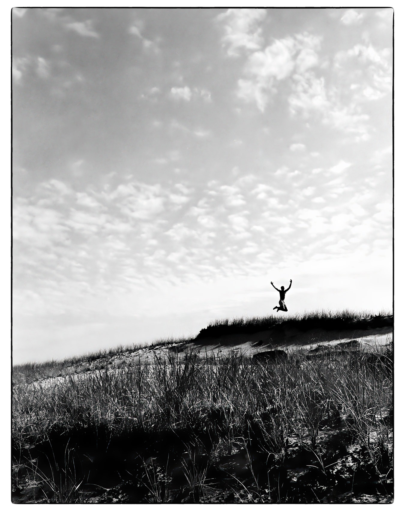 a-young-man-is-silhouetted-against-the-sky-as-he-jumps-off-a-sand-dune-in-provincetown-massachusetts