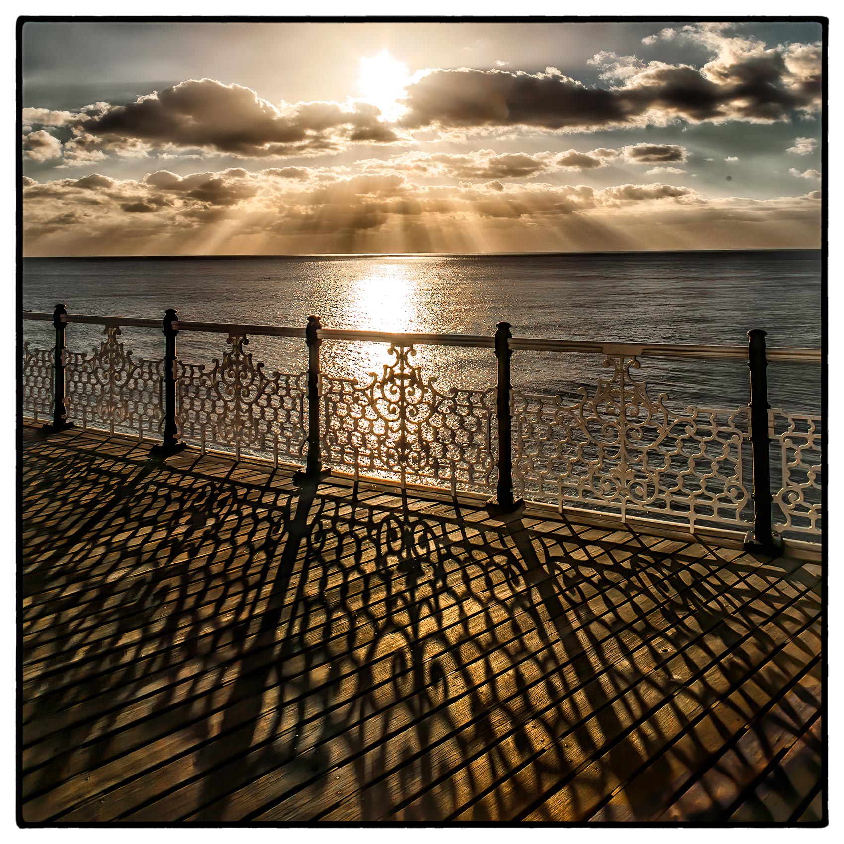 a brilliant sun breaks through the clouds  as it sets over brighton pier in southern england