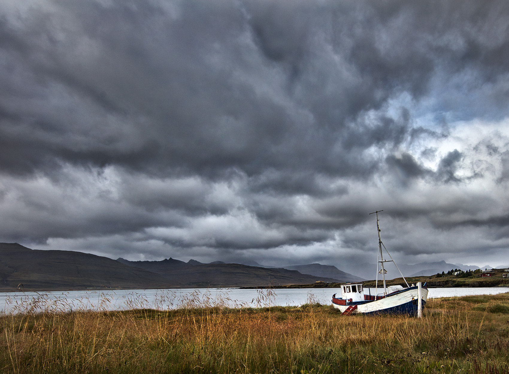 an abandoned icelandic fishing boat sits in an open field as the clouds roll in