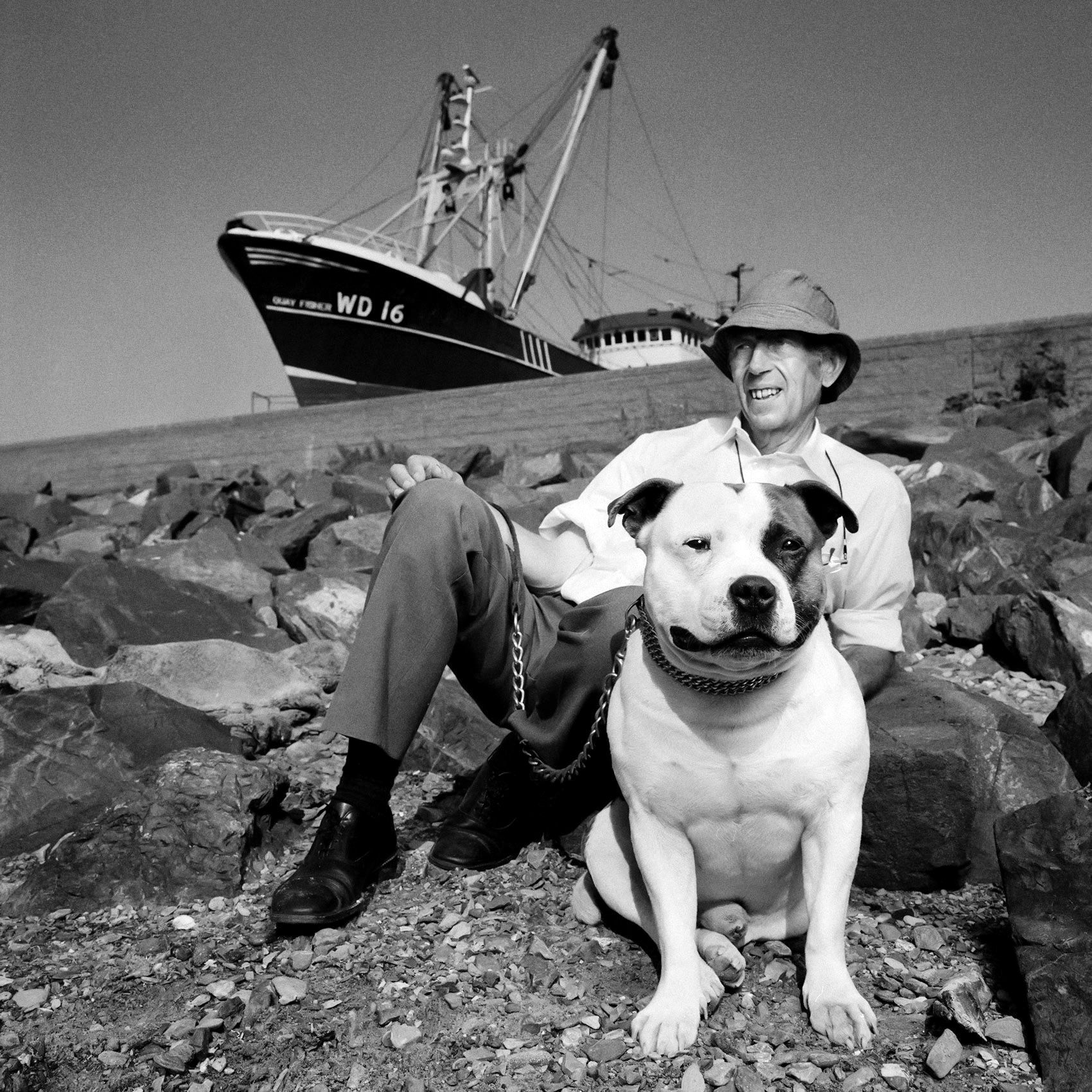 an-irishman-and-his-large-dog-sit-on-the-rocky-shoreline-in-howth-ireland