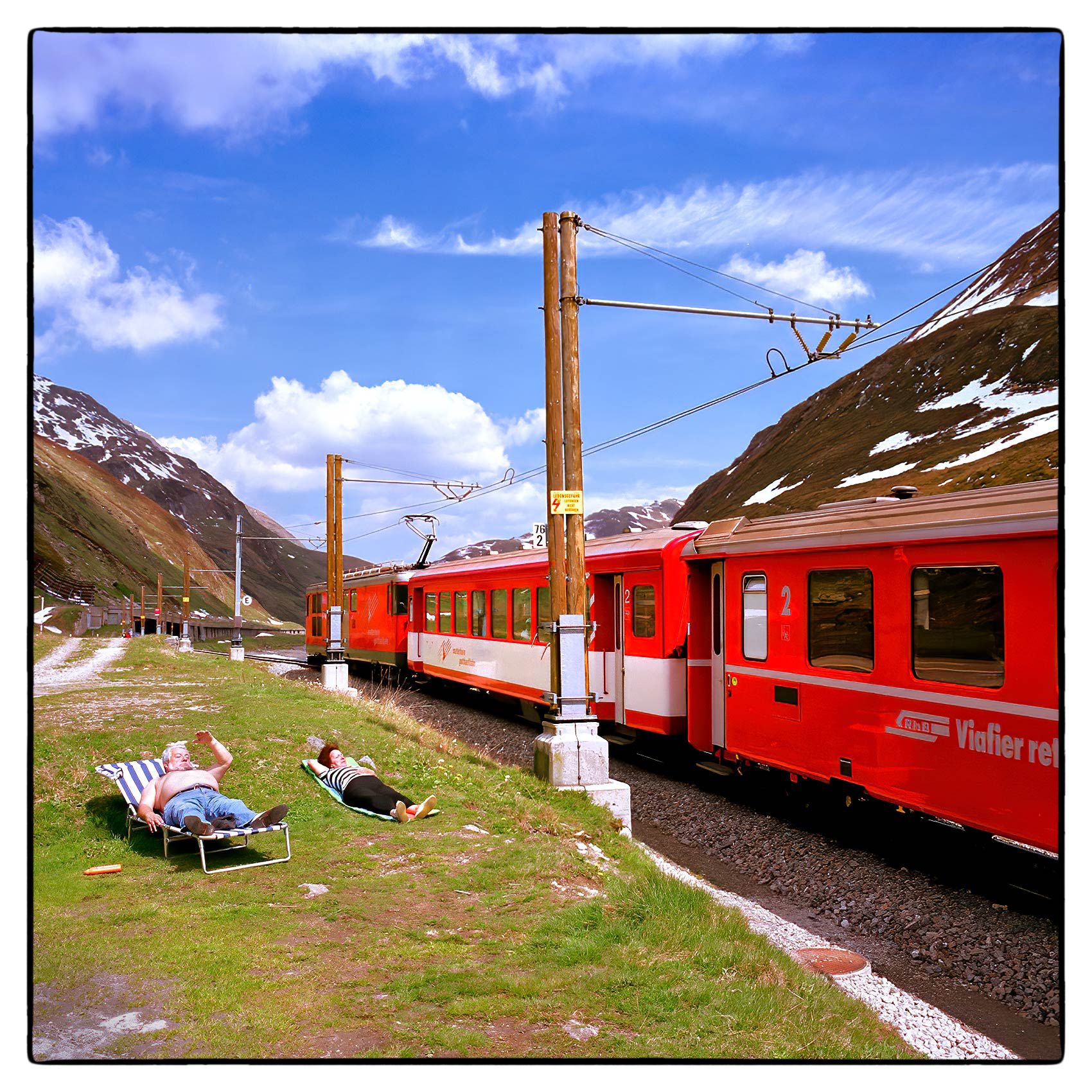 an-older-couple-suntan-next-to-the-train-tracks-high-in-the-swiss-alps