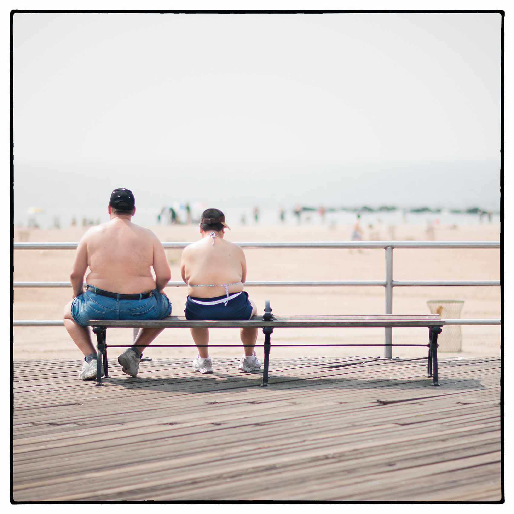 an-overweight-man-and-woman-sit-beside-each-other-on-the-boardwalk-at-coney-island
