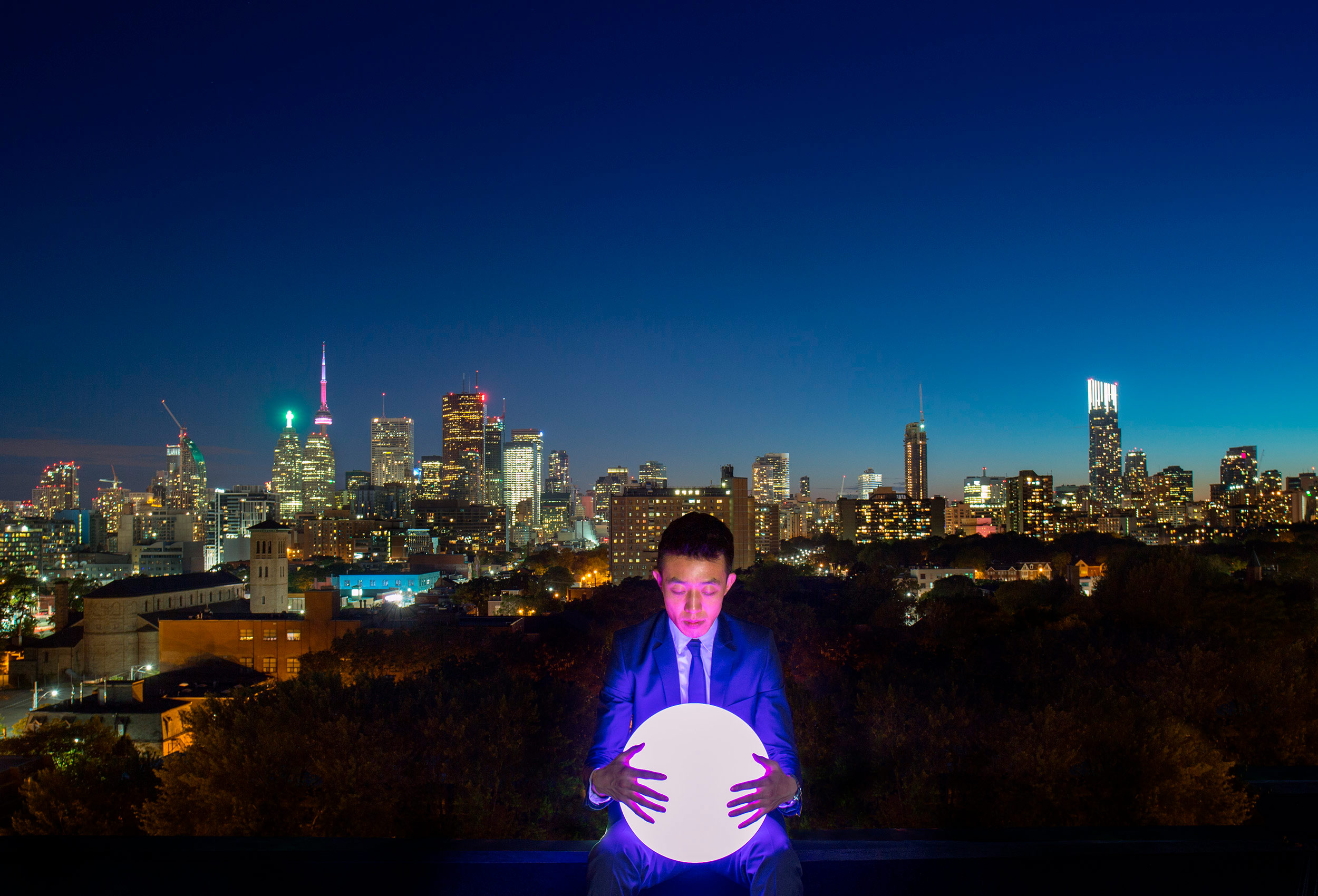 a man with a globe of light and the stunning  night skyline of toronto canada behind him