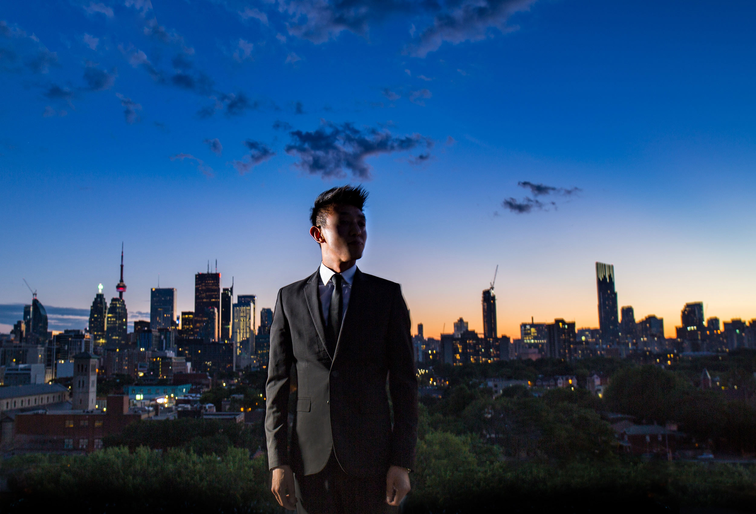 a man in a suit stands in front of the stunning toronto skyline at dusk