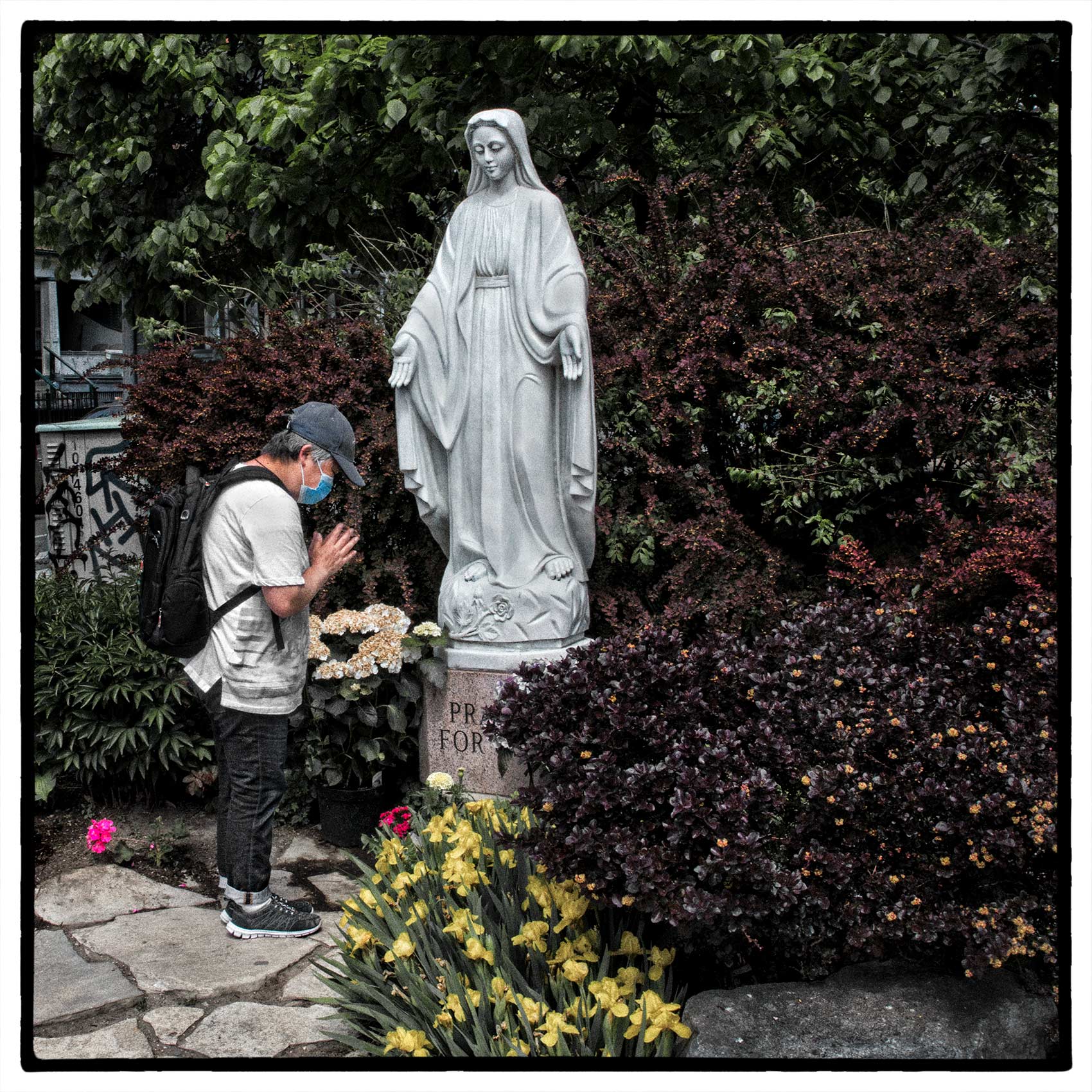 a woman prays to a statue of the Virgin Mary outside holy family church during the pandemic
