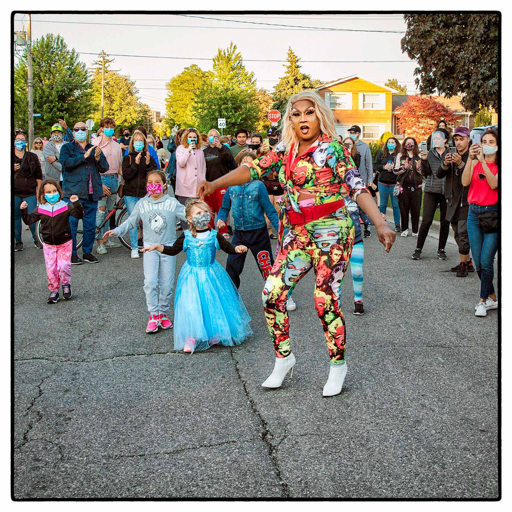 a colourful drag queen dances with children by Toronto photographer John Hryniuk