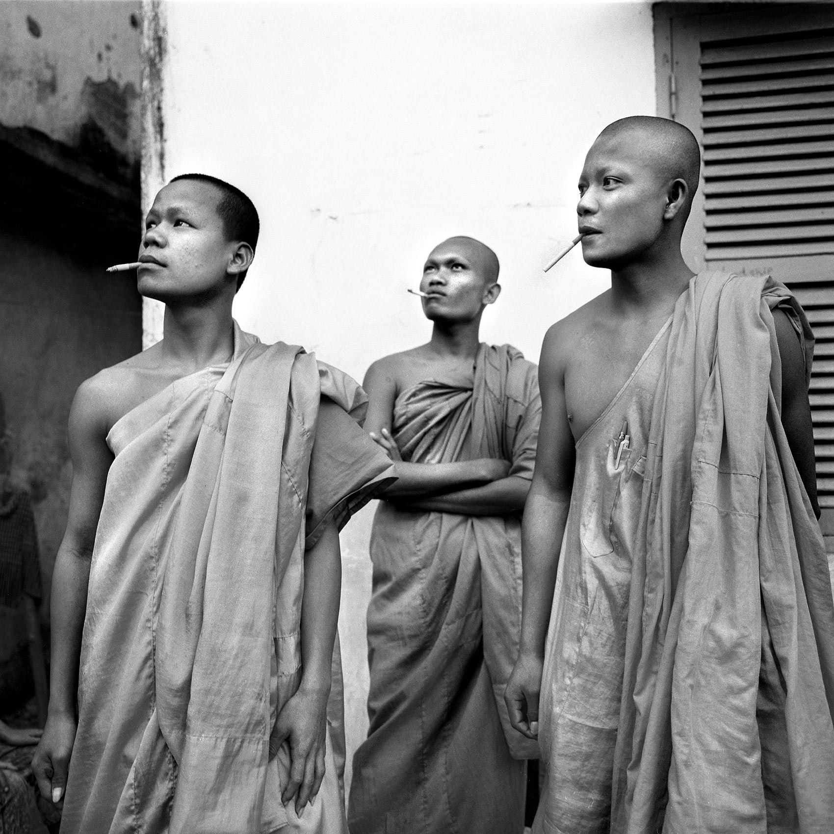 three monks pose for a photo as they smoke cigarettes in phnom penh cambodia