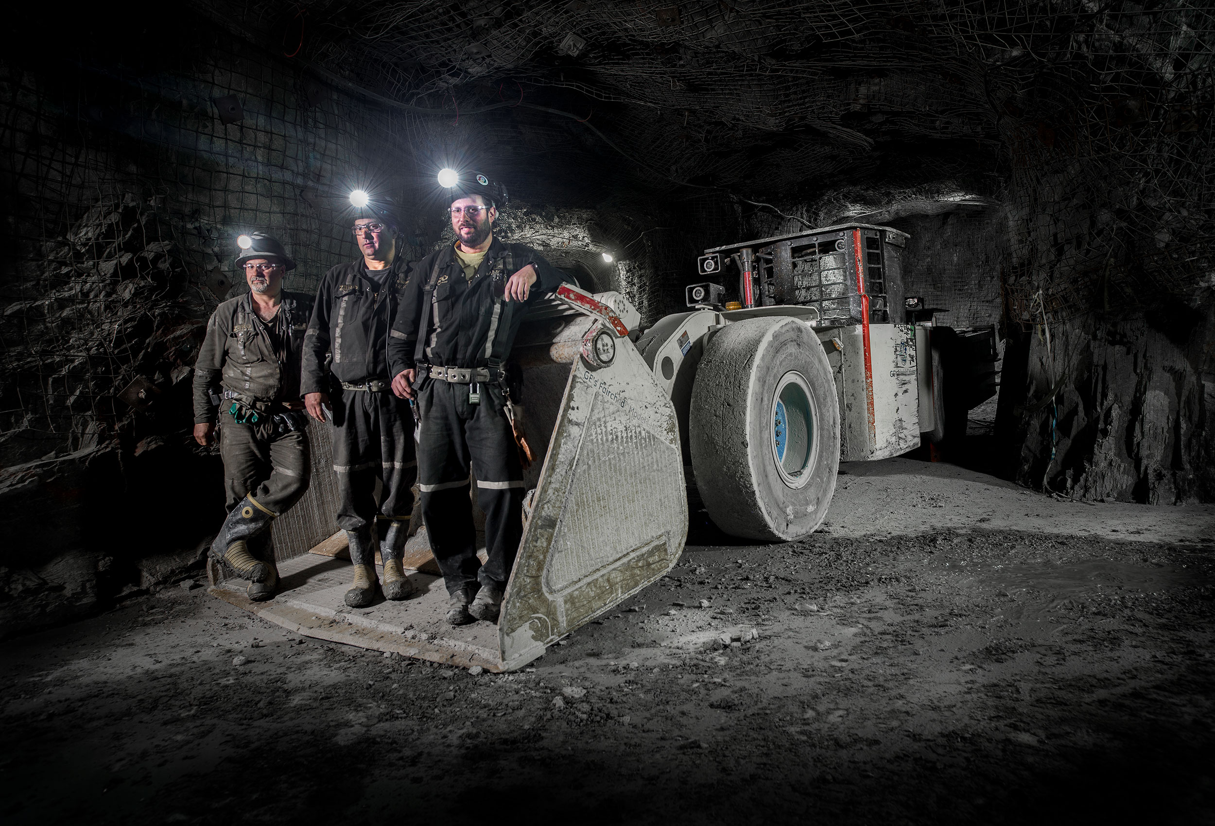 canadian miners pose for photography in front of an industrial atlas copco electric scooptram 