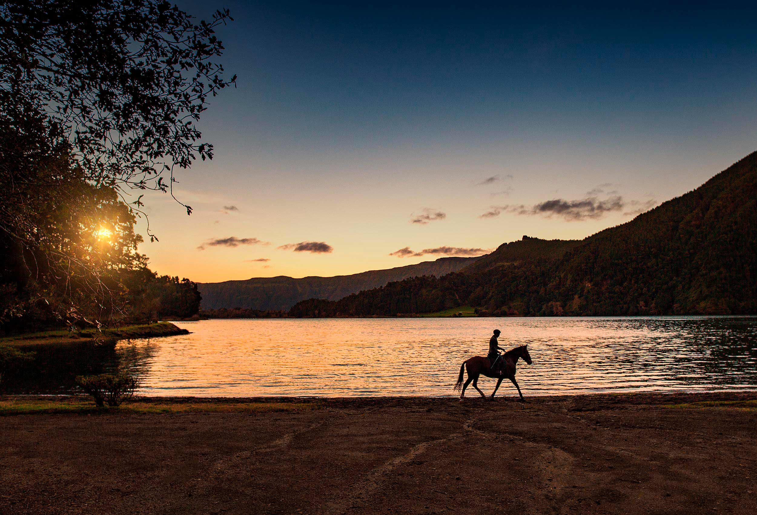 a horse back riders is sillhouetted against the setting sun on san miguel island in the azores