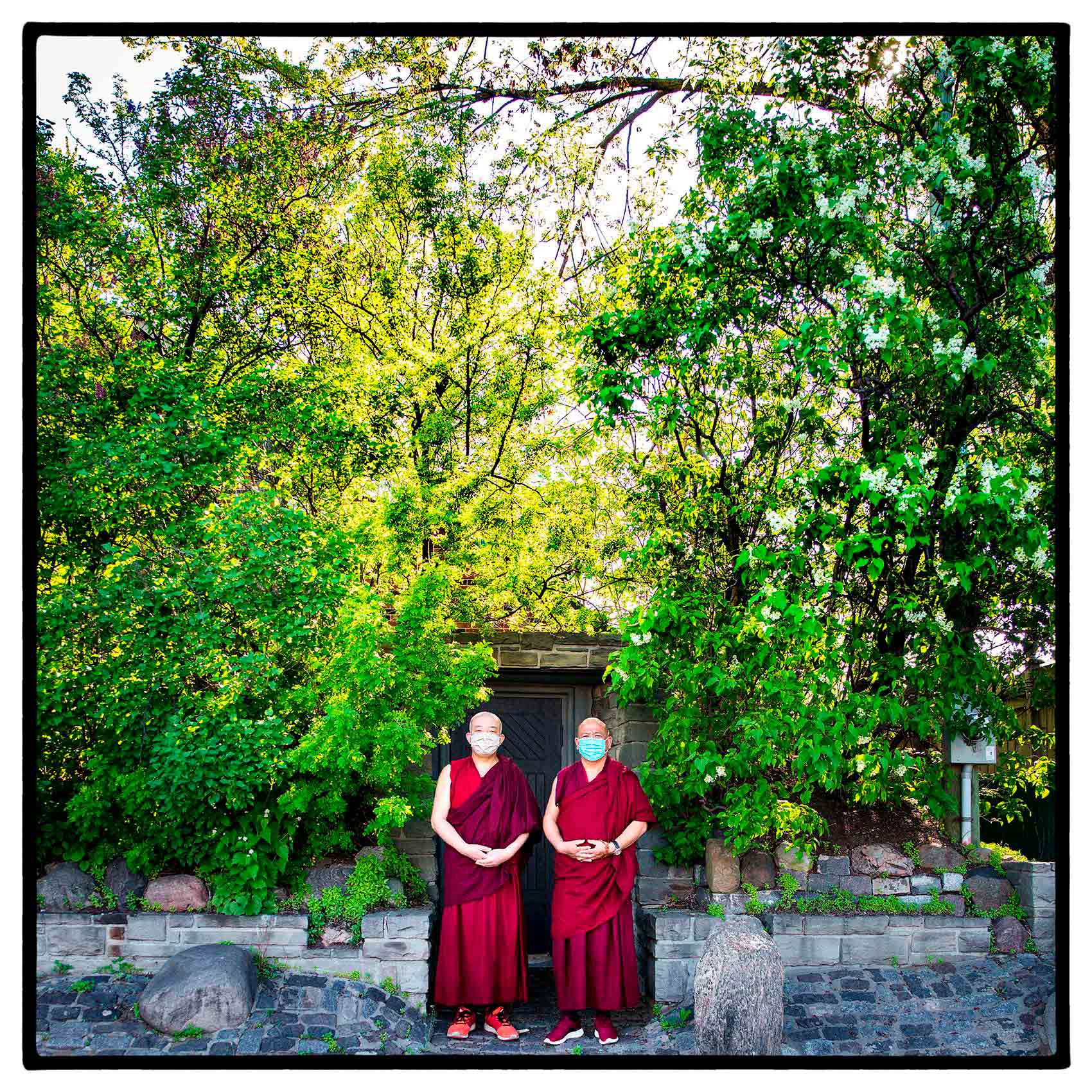 two tibetan monks in red dress and shoes with face masks pose for a photo during the pandemic