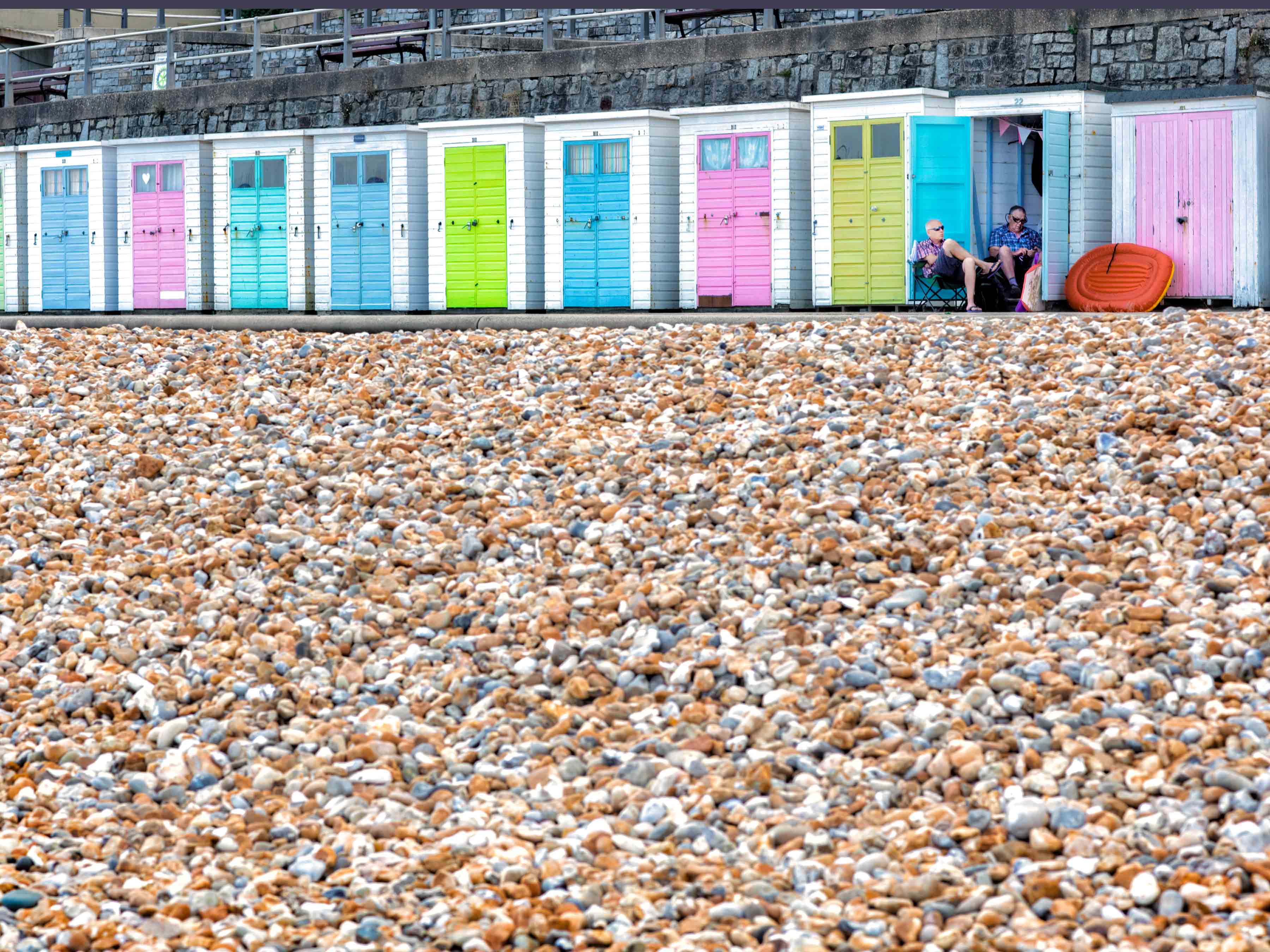 two men sit outside their colourful beach hut in the seaside town of lyme regis