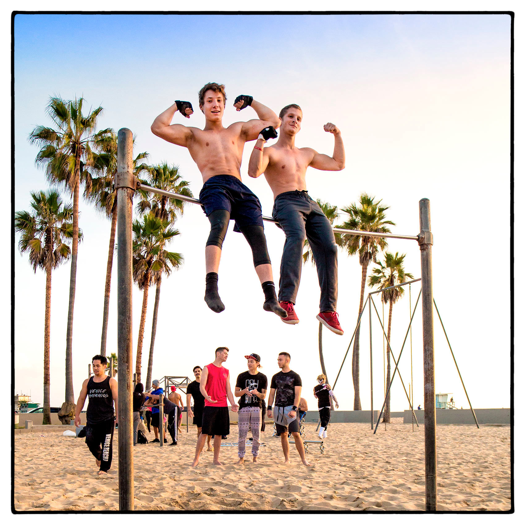 two-teenage-boys-show-off-their-muscles-while-sitting-on-a-parrallel-bar-in-venice-beach