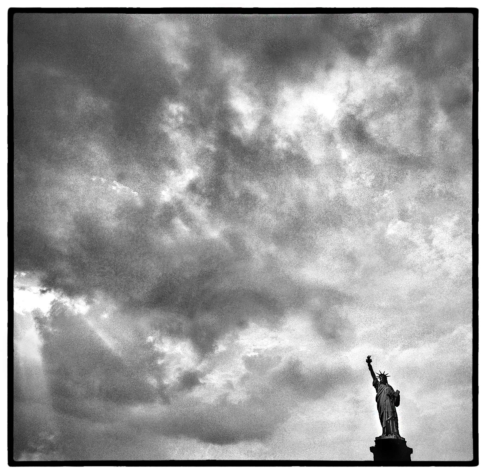 the sun breaks through the clouds over the statue of liberty in new york harbour